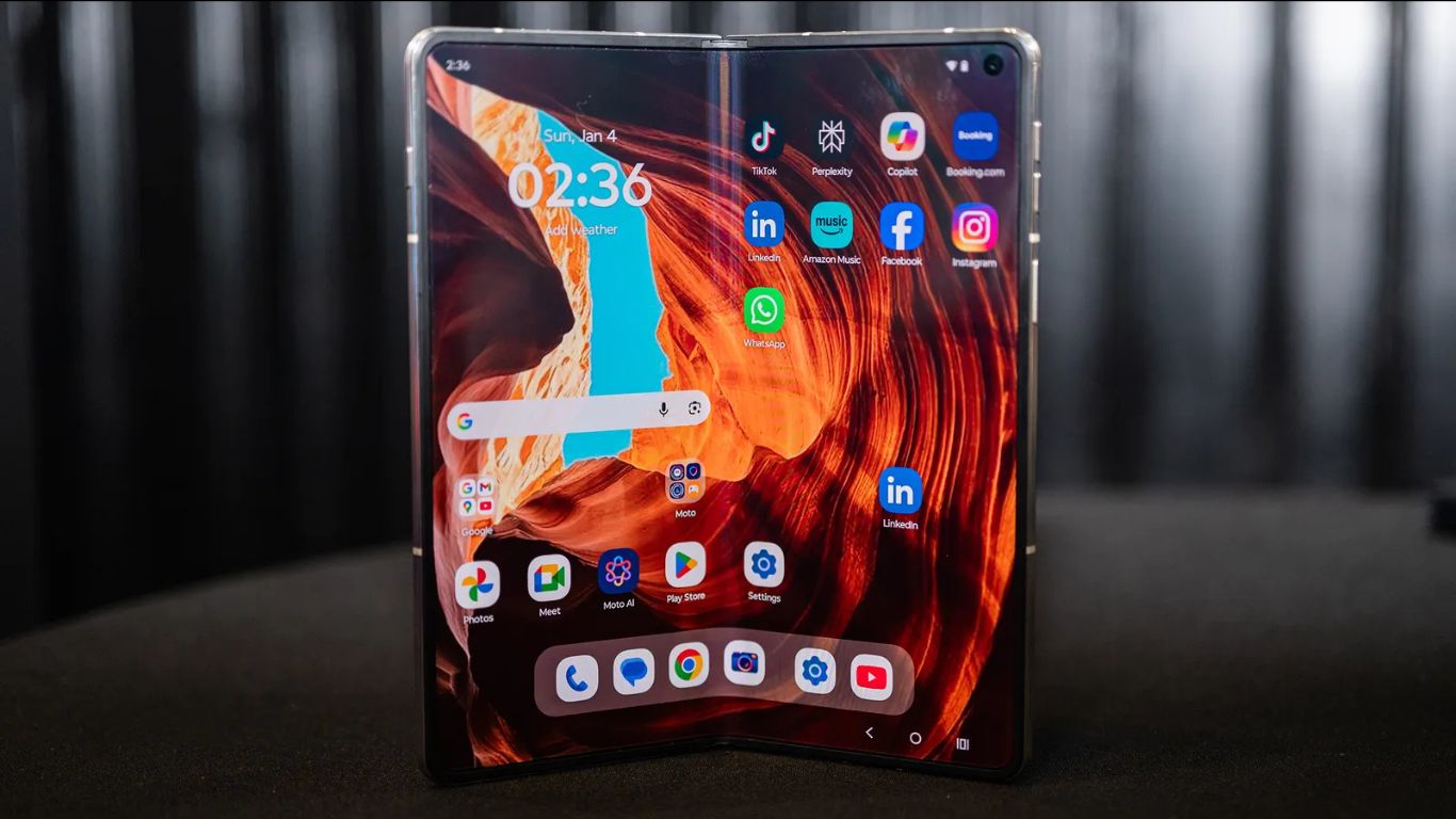 Motorola Razr Fold otvoren na stolu pored Moto Pen Ultra olovke sa prikazanim početnim ekranom